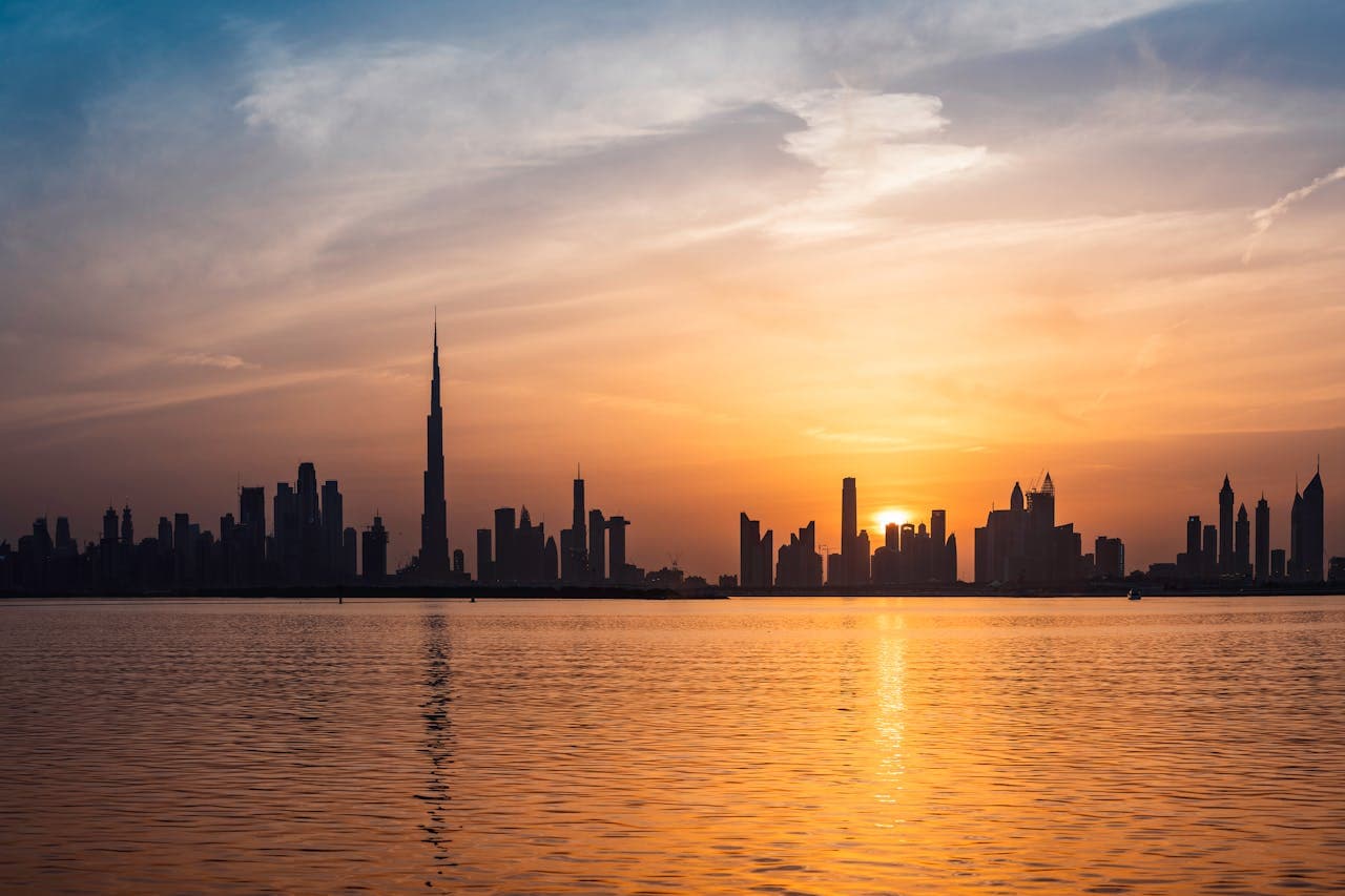 The Dubai skyline, with the Burj Khalifa, silhouetted against a sunset over the water