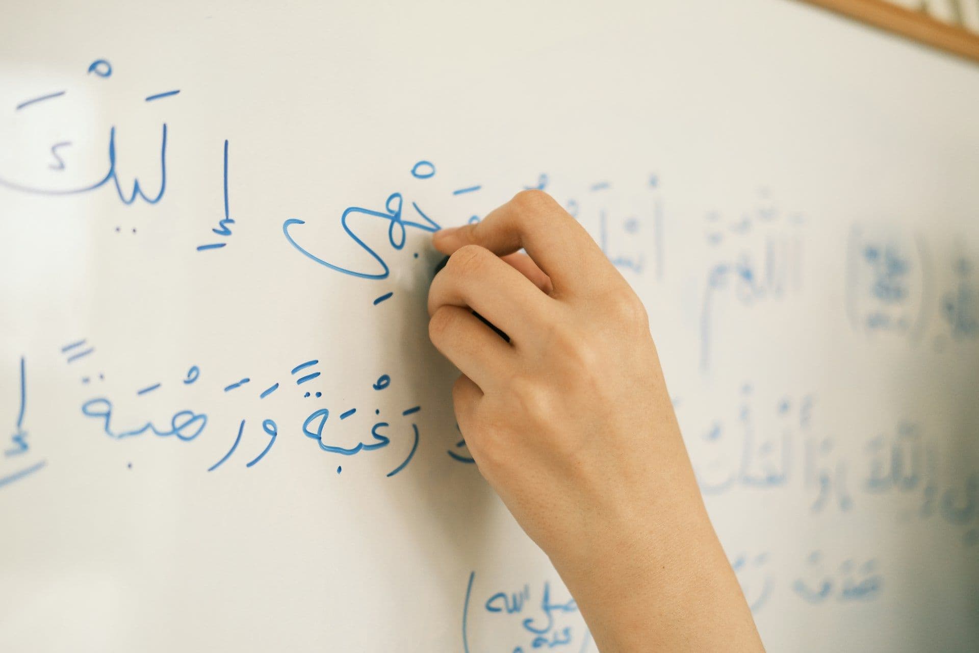 A hand writing Arabic script on a whiteboard