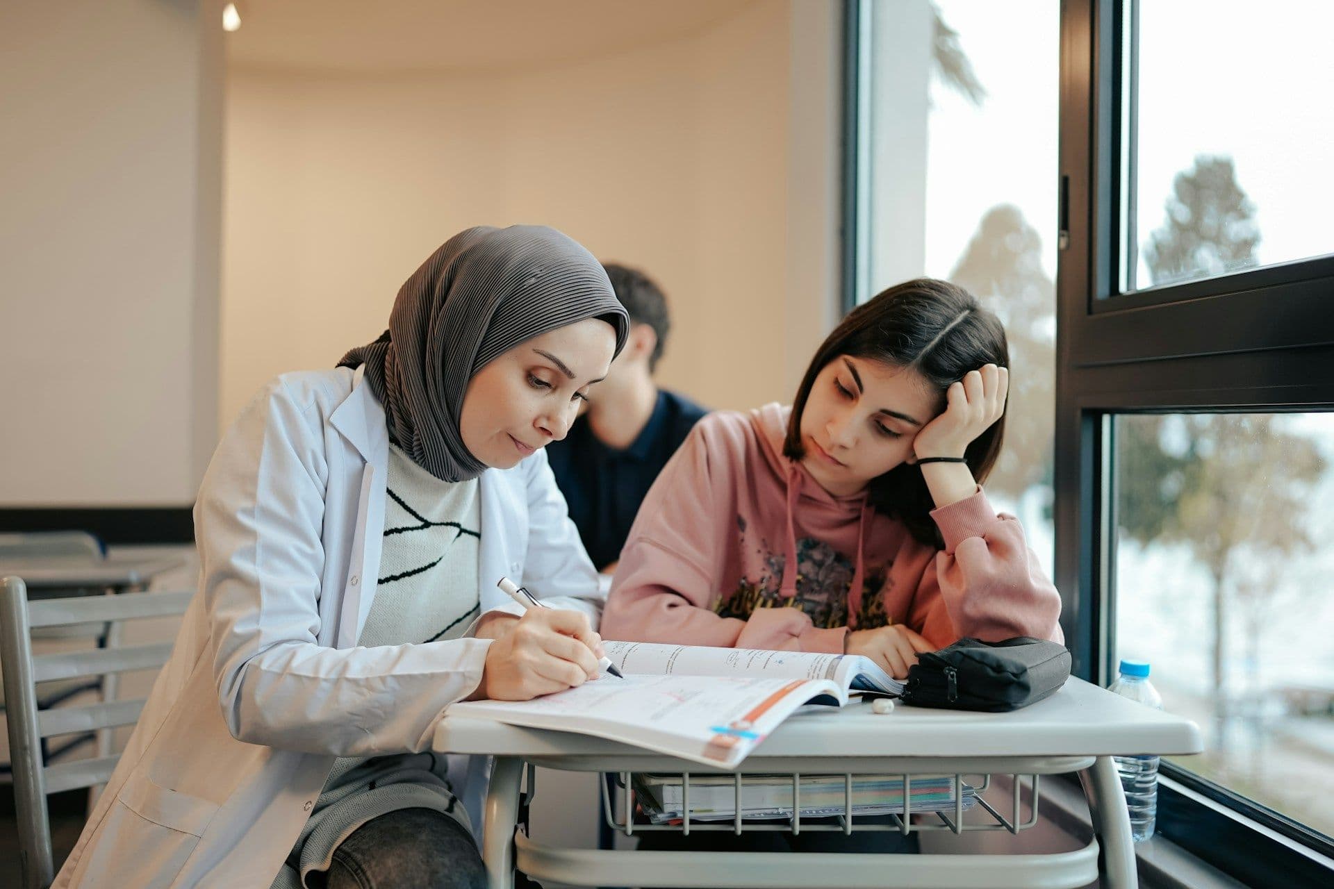 A teacher leaning over a desk to help a student with her work