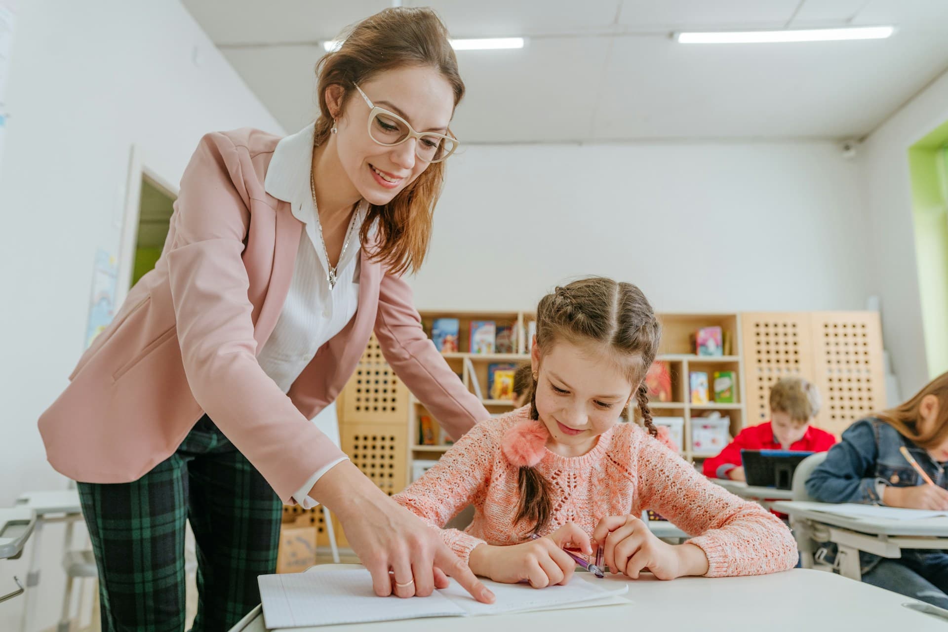 A teacher leaning in to help a smiling pupil with her work