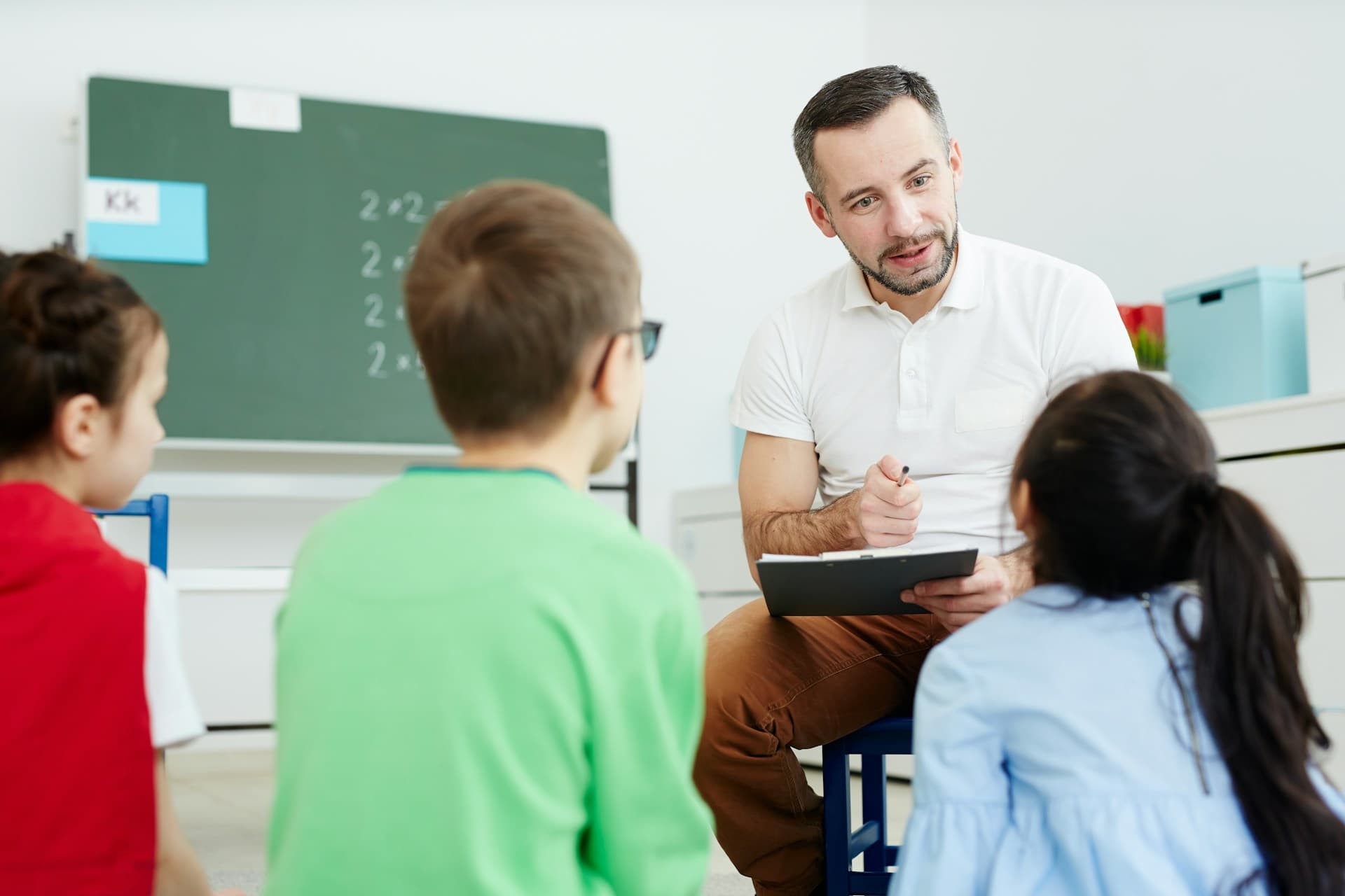 A teacher crouching beside a table to help a small group of primary pupils